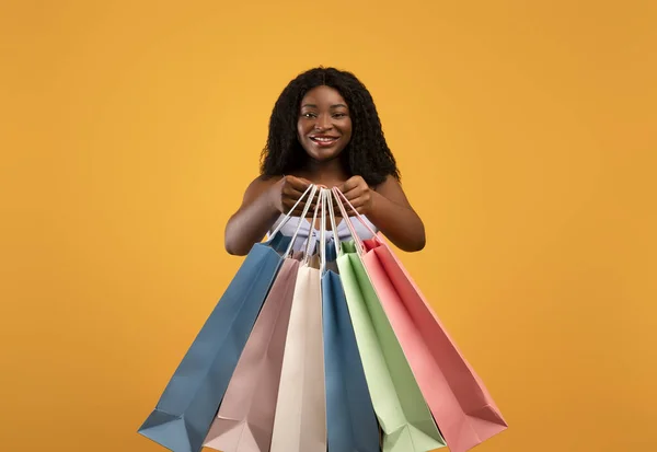 魅力的な若い黒人女性は、明るいショッピングバッグを保持し、オレンジのスタジオの背景上に販売で商品を購入 — ストック写真
