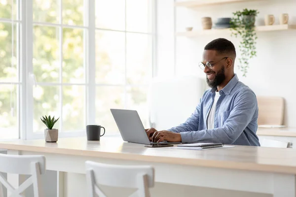 Glad millennial african american man with beard in glasses chatting remotely, work on computer alone — Zdjęcie stockowe