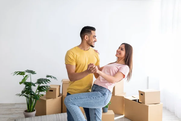 Happy millennial diverse couple dancing in their new home among cardboard boxes on relocation day, copy space —  Fotos de Stock