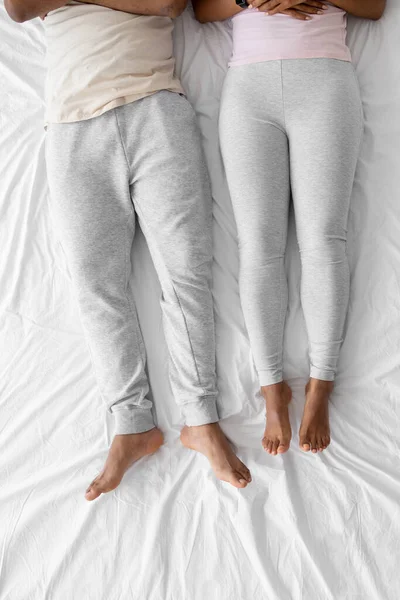 Millennial african american male and female lie on white bed in home clothes — Stockfoto