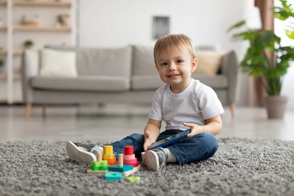 Happy little toddler boy watching cartoon on smartphone while sitting on floor carpet, looking and smiling at camera — Stockfoto