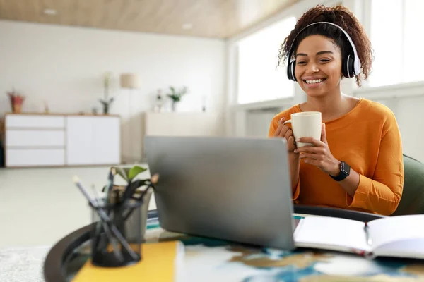 コンピュータでビデオを見ている黒人女性の笑顔,コーヒーを飲みます — ストック写真