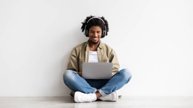 Happy Young African American Guy In Wireless Headphones Using Laptop