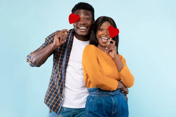 Jovens românticos casal preto cobrindo olhos com corações de papel vermelho — Fotografia de Stock