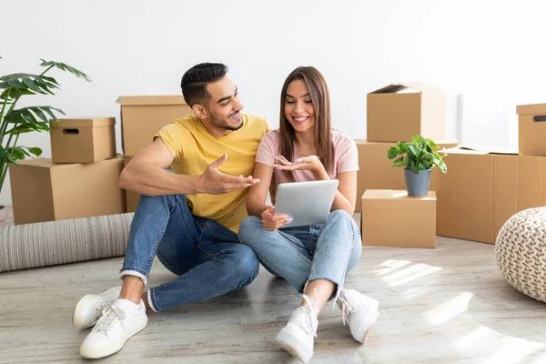 Married young diverse couple having online video call with relatives, sitting on floor among boxes on relocation day —  Fotos de Stock