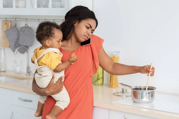 Stressed Young Black Woman Multitasking In Kitchen With Baby On Hands — Zdjęcie stockowe