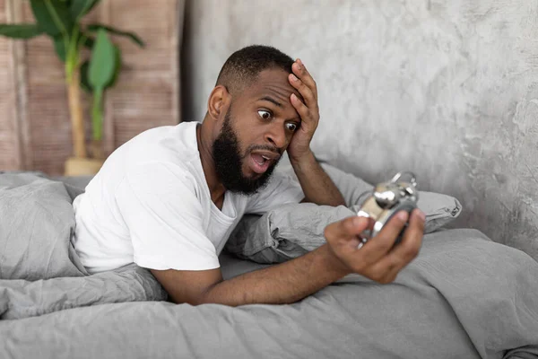 Hombre negro sorprendido mirando el reloj en la cama — Foto de Stock
