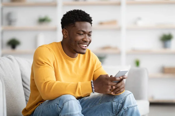 Handsome black guy chatting with girlfriend, using cellphone at home — Stock Fotó