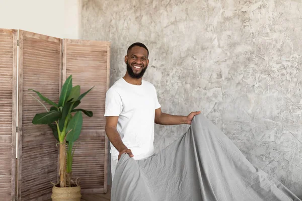 Smiling young African American man making bed in the morning — Fotografia de Stock