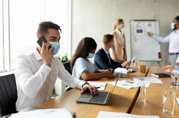 Arab Employee Wearing Mask Using Laptop And Cellphone During Meeting With Colleagues — Zdjęcie stockowe