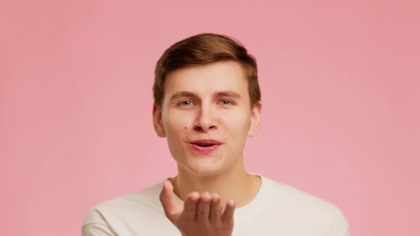 Грайливий хлопець дме поцілунок усміхнений позує над рожевим тлом — стокове відео