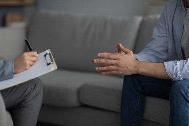 Unrecognizable psychologist supporting male patient, writing on clipboard at medical office, closeup, crop