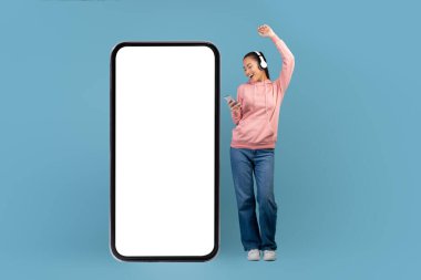Cheerful young asian woman with headset and smartphone dancing
