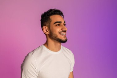 Handsome happy young Arab man in white t-shirt looking aside and smiling in neon light, copy space