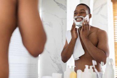 Shaving Routine. Shirtless Black Man Applying Shave Foam On Face In Bathroom