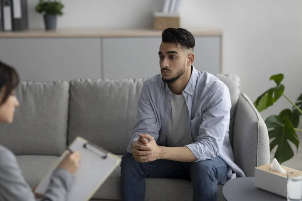 Upset arab man suffering from depression, counselor providing professional assistance at clinic office — Stockfoto