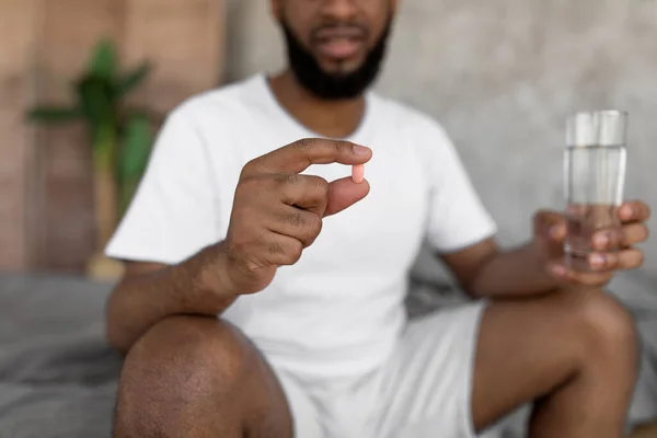Чорний чоловік приймає таблетки, тримаючи склянку води — стокове фото