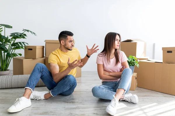 Unhappy young multiracial couple having argument, sitting on floor in their new apartment on moving day — Fotografia de Stock