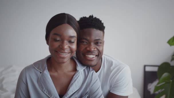 Νεαρό ζευγάρι Αφροαμερικανών ερωτευμένων φορώντας πιτζάμες χαμογελώντας ειλικρινά στην κάμερα, αγκαλιασμένοι στο σπίτι — Αρχείο Βίντεο