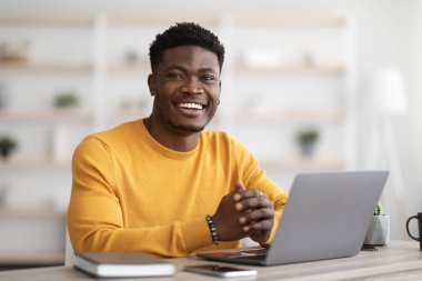 Portrait of positive black guy working on laptop