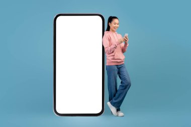 Millennial chinese woman standing by huge cellphone, using mobile app