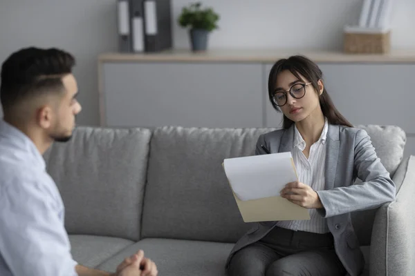 Psychotherapy concept. Focused female psychotherapist interviewing young man, listening and taking notes — Stockfoto