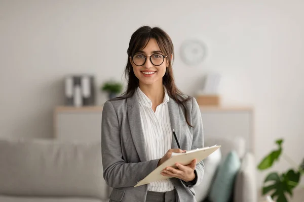 Happy professional middle eastern female psychologist looking and smiling at camera, working in modern office