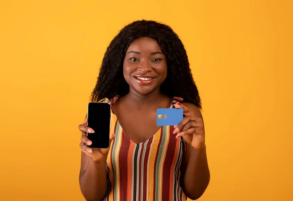 Новий чудовий мобільний додаток для покупок. Весела чорна жінка показує мобільний телефон з порожнім екраном і кредитною карткою — стокове фото