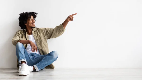 Check This. Positive African American Guy Sitting On Floor And Pointing Aside — Stockfoto