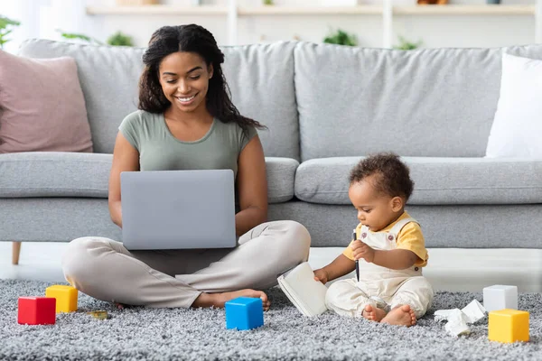 Remote Job. Young Black Mother Using Laptop And Taking Care About Baby — стоковое фото