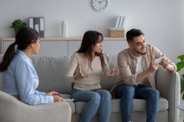 Smartphone addiction. Arab wife complaining to family counselor about her careless spouse busy with cellphone game