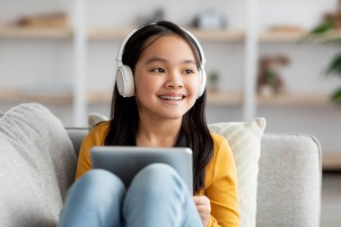 Excited asian kid using wireless headset and digital tablet