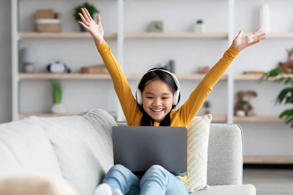 Emotional asian girl with wireless headset using laptop at home — Fotografia de Stock