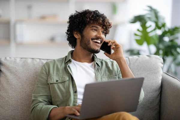 Happy handsome indian guy working online, having phone conversation