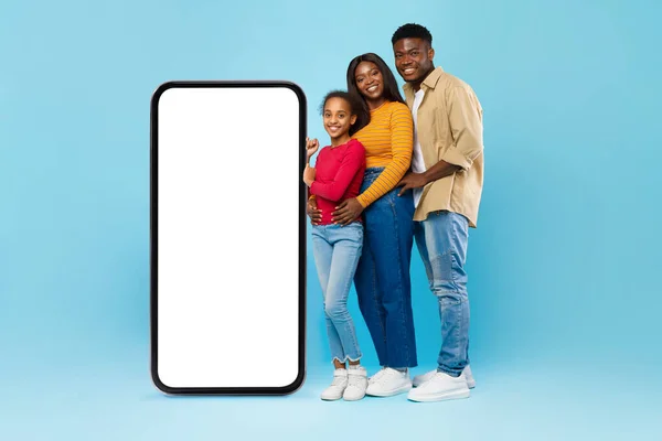 Black family presenting white empty smartphone leaning on big screen — 图库照片