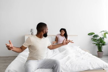 Despaired angry excited young black wife and husband freaking out and yells, swear in bedroom interior, copy space