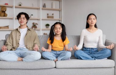 Calm teen girl, millennial korean guy and lady with closed eyes sit on sofa in lotus position, practice yoga
