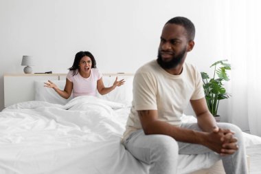 Sad young black man listen wife, woman freaking out and yells at unhappy husband, swear in bedroom interior