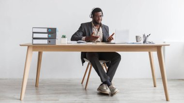 Young black businessman making video call, using laptop at office, having web conference with clients against white wall