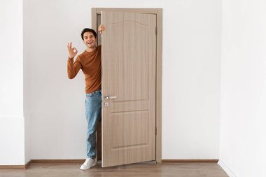 Cheerful guy looking out of door showing okay sign gesture