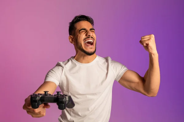 Excited Arab guy winning online esports competition, playing video game, shouting OMG, making YES gesture in neon light — Stok fotoğraf