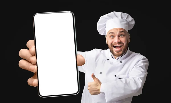 Overjoyed professional chef showing phone with big empty screen and gesturing thumb up, mockup, closeup — Fotografia de Stock