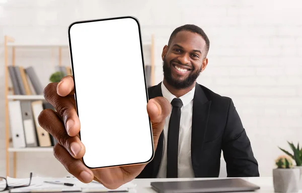 Happy african american businessman showing cellphone with big blank screen at office, mockup for app or website design — Foto Stock