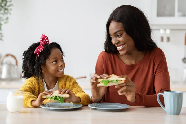 Lunch Together. Little Black Girl And Her Mother Eating Sandwiches In Kitchen — Foto de Stock