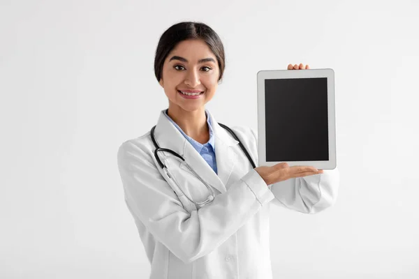 Happy young attractive indian female medical worker in uniform shows digital tablet with blank screen — Stock Photo, Image