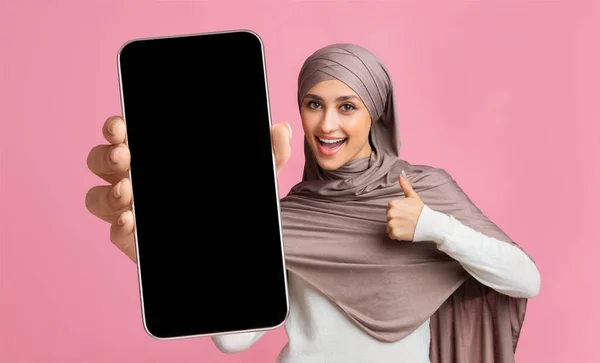 Wanita arab yang bersemangat menampilkan smartphone dengan layar kosong besar dan jempol ke atas, menunjukkan ruang kosong untuk aplikasi atau situs web — Stok Foto