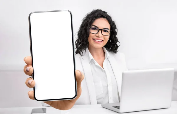 Médico femenino mostrando un gran smartphone con pantalla en blanco, sentado en la oficina en el lugar de trabajo, primer plano, maqueta — Foto de Stock