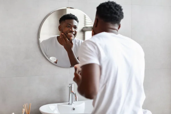 Feliz chico negro aplicando crema hidratante en la cara en el baño — Foto de Stock