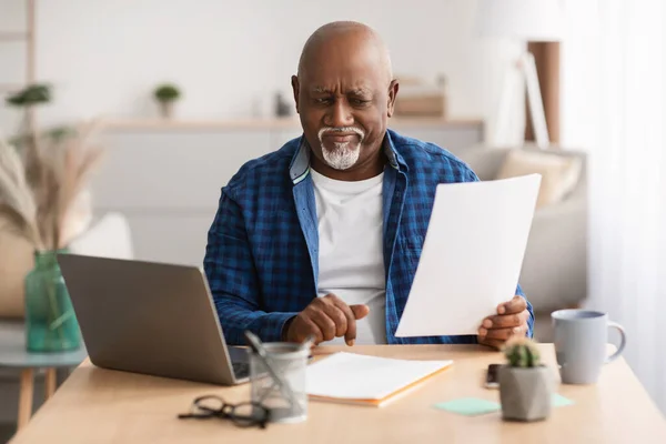 不満を持つ高齢黒人ビジネスマン職場で座ってビジネス論文を読む — ストック写真