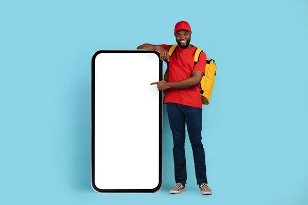 Order Online. Black Delivery Guy With Thermal Backpack Pointing At Blank Smartphone — 图库照片